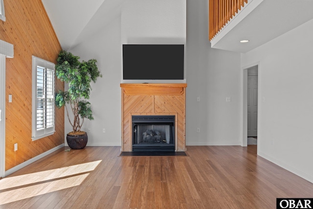 unfurnished living room featuring wood finished floors, baseboards, high vaulted ceiling, wood walls, and a tiled fireplace