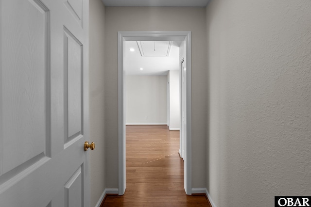 hallway featuring attic access, a textured wall, dark wood-type flooring, and baseboards