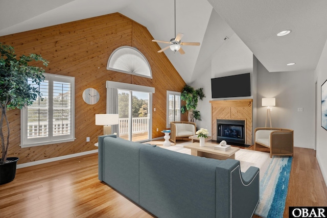 living area with a tiled fireplace, wood finished floors, wood walls, and high vaulted ceiling