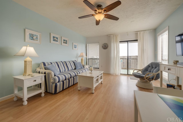 living area featuring a textured ceiling, light wood-type flooring, a ceiling fan, and baseboards