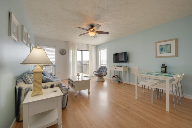 living area featuring a textured ceiling, light wood-style flooring, baseboards, and ceiling fan