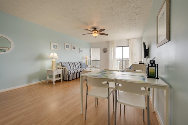 dining area featuring a textured ceiling, baseboards, light wood finished floors, and ceiling fan