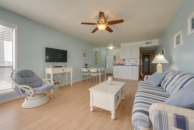 living area with visible vents, baseboards, light wood-type flooring, and ceiling fan