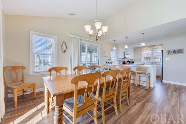 dining space with baseboards, visible vents, lofted ceiling, light wood-style floors, and a notable chandelier