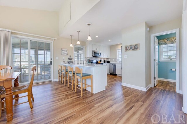 kitchen featuring stainless steel appliances, a kitchen breakfast bar, white cabinets, light countertops, and decorative light fixtures