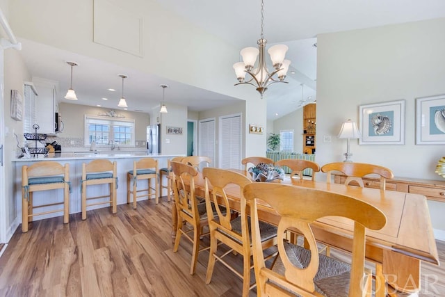 dining room with light wood-type flooring, a notable chandelier, and vaulted ceiling