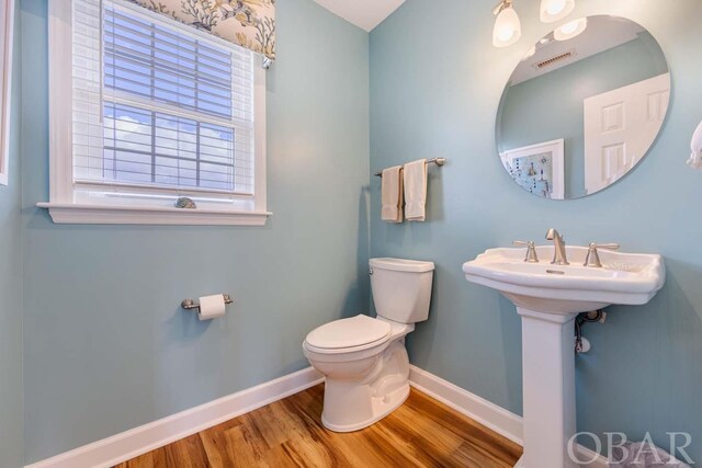 half bath featuring toilet, visible vents, baseboards, and wood finished floors