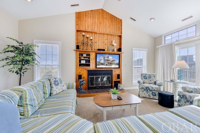 carpeted living area featuring high vaulted ceiling, a glass covered fireplace, and visible vents