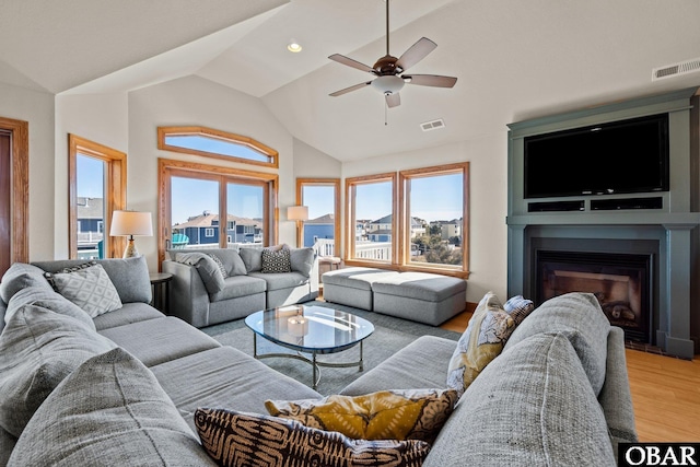 living room featuring a glass covered fireplace, visible vents, lofted ceiling, and wood finished floors