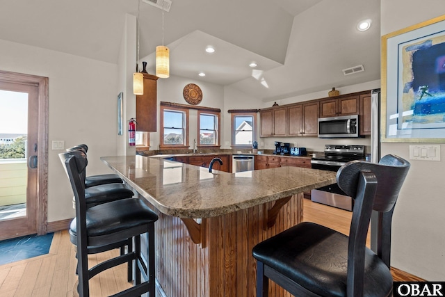 kitchen featuring a breakfast bar, visible vents, vaulted ceiling, appliances with stainless steel finishes, and decorative light fixtures