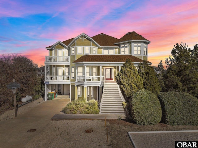 view of front of property featuring a balcony, a shingled roof, driveway, stairway, and a carport