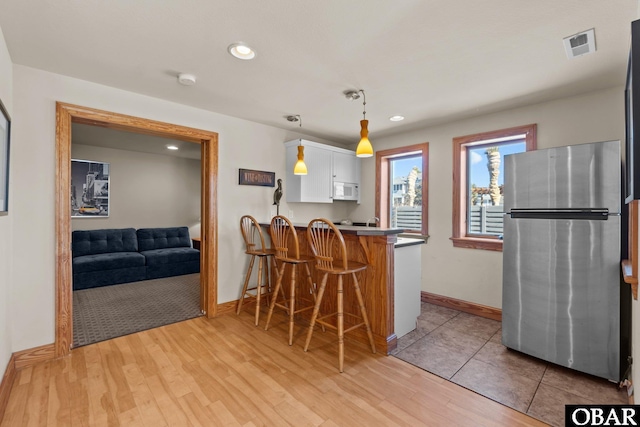 kitchen with hanging light fixtures, white microwave, freestanding refrigerator, a peninsula, and a kitchen breakfast bar