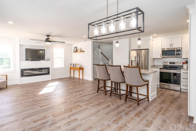 kitchen featuring stainless steel appliances, hanging light fixtures, white cabinets, light stone countertops, and a kitchen breakfast bar