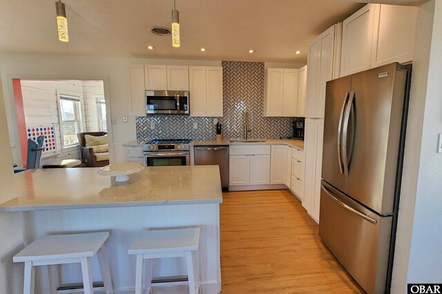 kitchen with stainless steel appliances, a peninsula, a sink, white cabinets, and hanging light fixtures