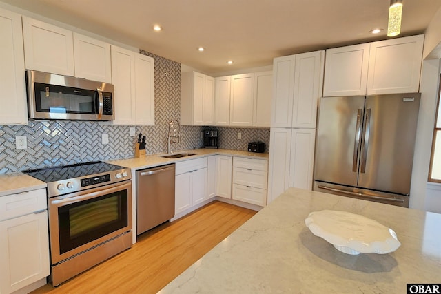 kitchen with appliances with stainless steel finishes, a sink, white cabinetry, and light stone countertops