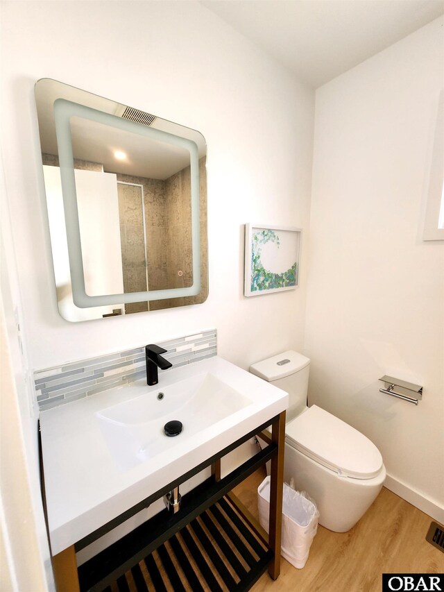 bathroom featuring baseboards, decorative backsplash, toilet, wood finished floors, and a sink