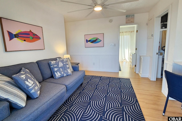 living room with a textured ceiling, wainscoting, wood finished floors, and a ceiling fan