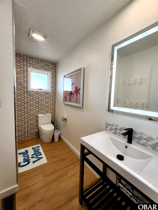 bathroom with visible vents, toilet, a textured ceiling, wood finished floors, and baseboards