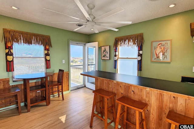 interior space featuring light wood finished floors, a ceiling fan, a textured ceiling, a bar, and recessed lighting