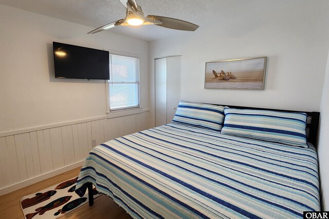 bedroom featuring a textured ceiling, a wainscoted wall, wood finished floors, a ceiling fan, and a closet