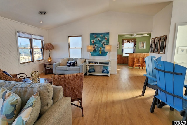 living area with wooden walls, visible vents, a wainscoted wall, vaulted ceiling, and light wood-type flooring