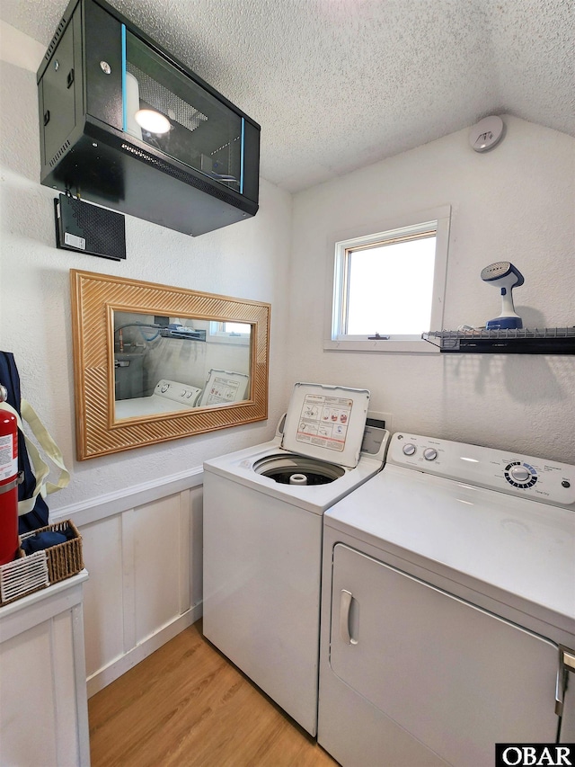 clothes washing area with laundry area, light wood finished floors, a textured ceiling, and washing machine and clothes dryer