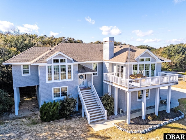 view of front of house with a shingled roof, a chimney, a deck, and stairs