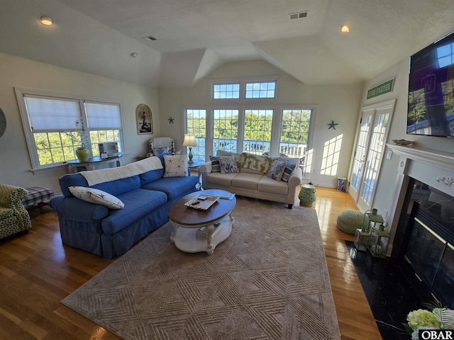 living room featuring a glass covered fireplace, plenty of natural light, wood finished floors, and visible vents