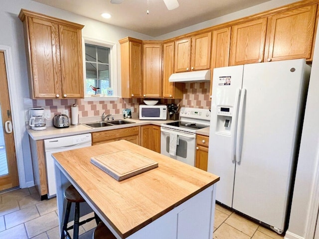 kitchen with butcher block countertops, a sink, under cabinet range hood, backsplash, and white appliances