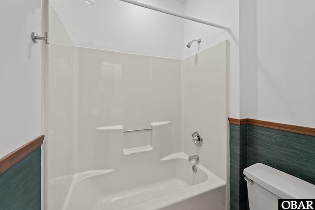 bathroom featuring  shower combination, a wainscoted wall, and toilet