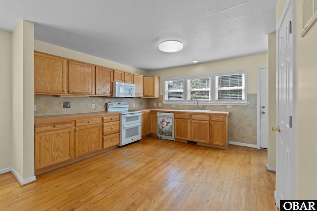 kitchen featuring white appliances, light wood finished floors, wainscoting, light countertops, and a sink