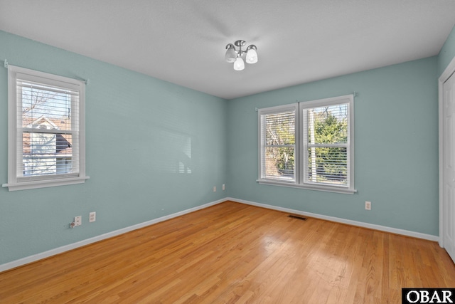 empty room with light wood-style floors, visible vents, and baseboards