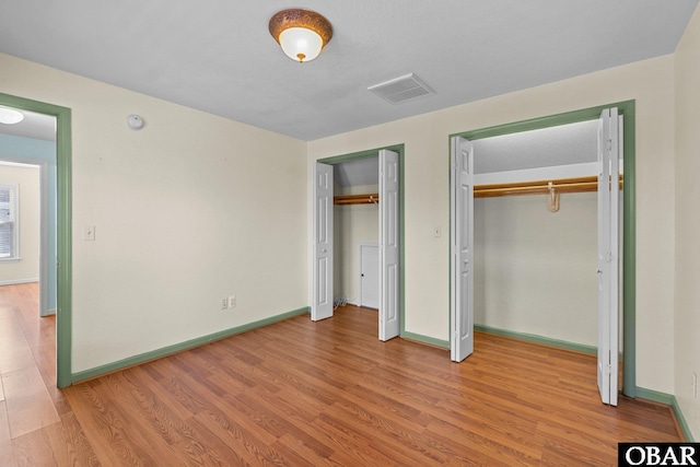 unfurnished bedroom with baseboards, light wood-style flooring, visible vents, and multiple closets