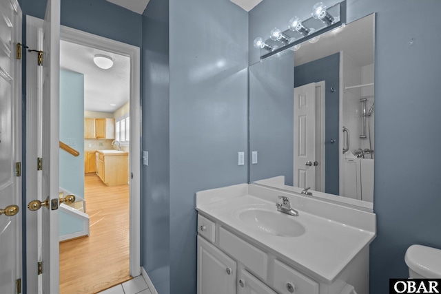 bathroom featuring toilet, a shower, wood finished floors, and vanity