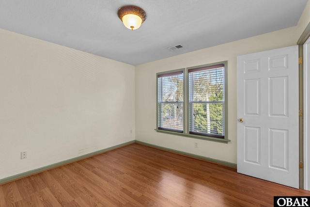 empty room with baseboards, visible vents, and wood finished floors