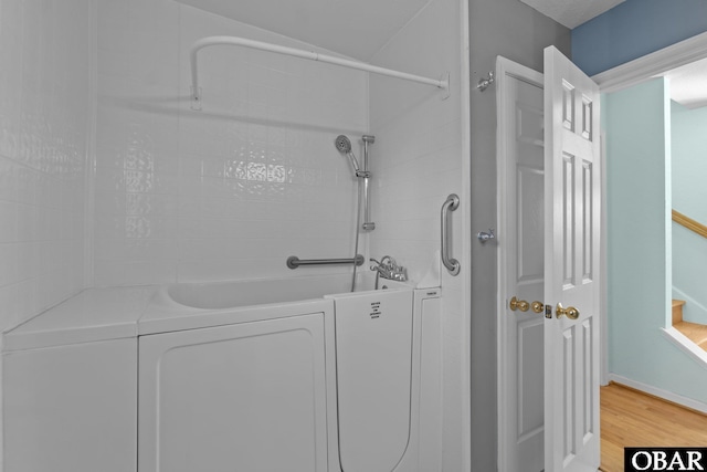 bathroom featuring washtub / shower combination, washer / clothes dryer, and wood finished floors