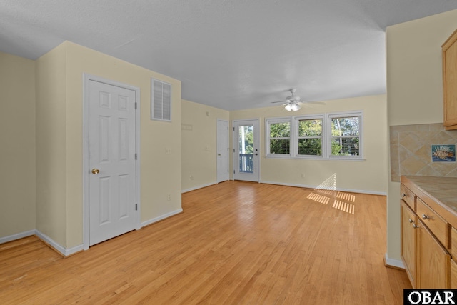 unfurnished living room with light wood-style floors, baseboards, visible vents, and a ceiling fan