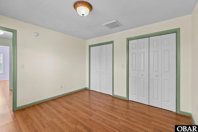 unfurnished bedroom with light wood finished floors, two closets, visible vents, and baseboards