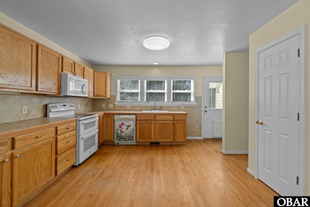 kitchen featuring tile countertops, white appliances, a sink, light wood-style floors, and decorative backsplash