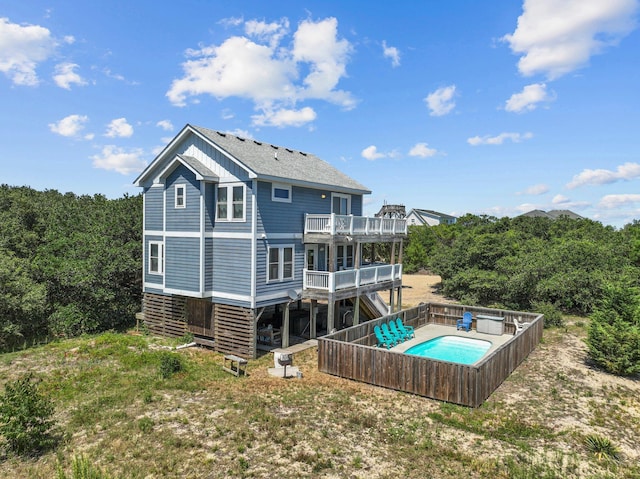 back of property with a balcony, a deck, a fenced in pool, and roof with shingles