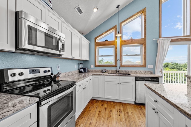 kitchen with a sink, white cabinetry, appliances with stainless steel finishes, light stone countertops, and decorative light fixtures