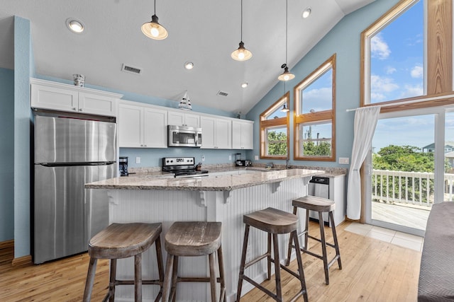 kitchen featuring a breakfast bar area, light stone counters, stainless steel appliances, white cabinetry, and pendant lighting