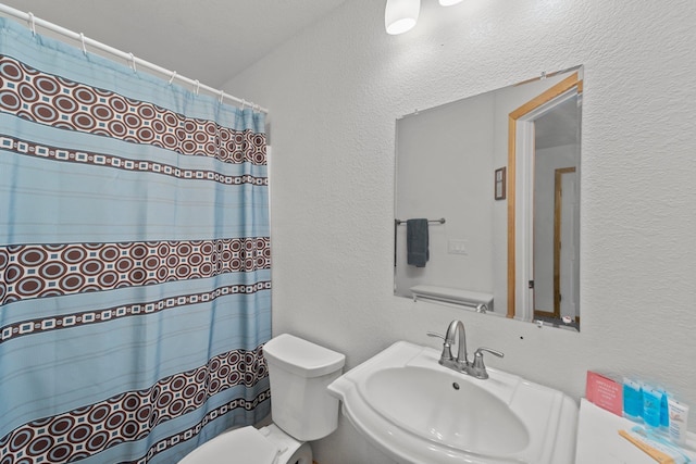 full bathroom with a textured wall, a shower with curtain, a sink, and toilet