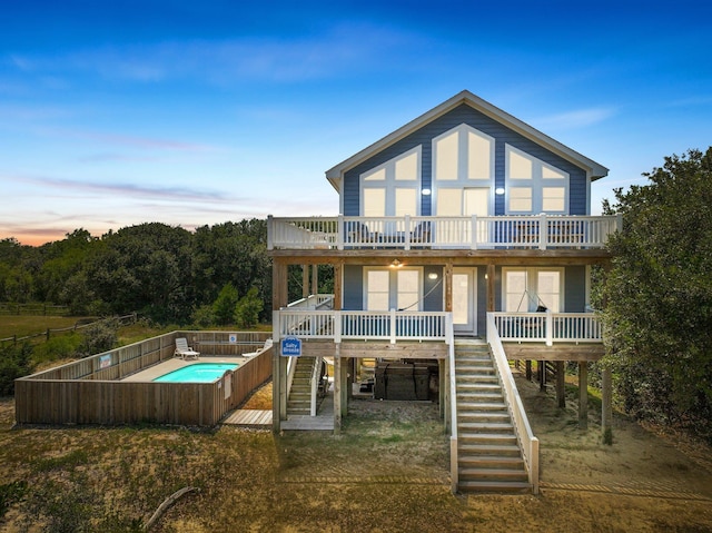 back of house at dusk with stairs, a deck, a fenced in pool, and french doors