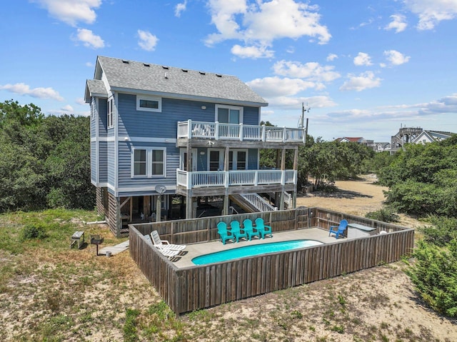 back of house featuring roof with shingles, stairway, a balcony, and a fenced in pool