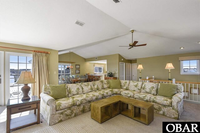 living area featuring light carpet, vaulted ceiling, visible vents, and a ceiling fan