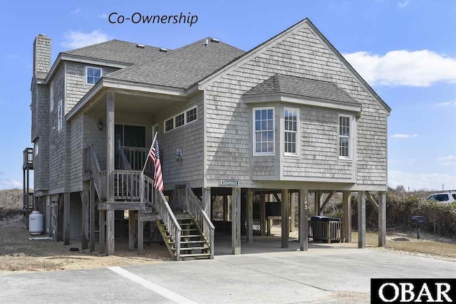 coastal home with a shingled roof, a chimney, driveway, and a carport