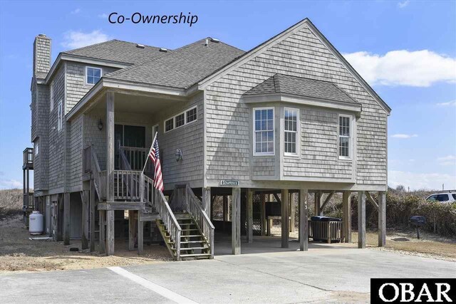 coastal home with a shingled roof, a chimney, driveway, and a carport