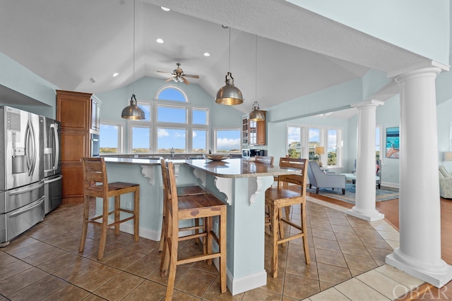 kitchen featuring brown cabinets, a breakfast bar area, stainless steel fridge, and ornate columns