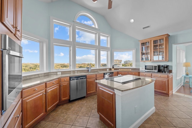 kitchen featuring a center island, light tile patterned floors, appliances with stainless steel finishes, glass insert cabinets, and a sink